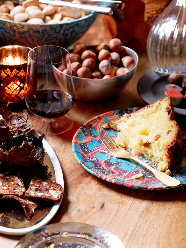 Still life of an ornate table with sliced cake, wine, nuts, and chocolates illuminated by a candle for an atmospheric holiday meal.