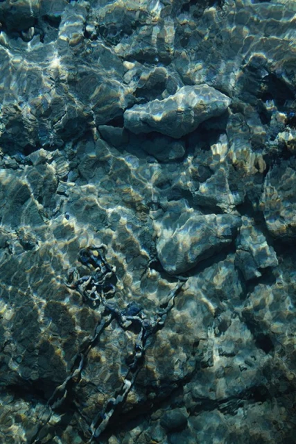 Underwater view of rocks and shimmering light patterns on a seabed, creating a textured and tranquil aquatic scene.