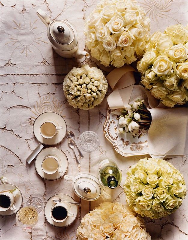 Overhead shot of a tea set, flower bouquets, serving tray, and glassware on a textured tablecloth, creating an elegant and inviting scene.