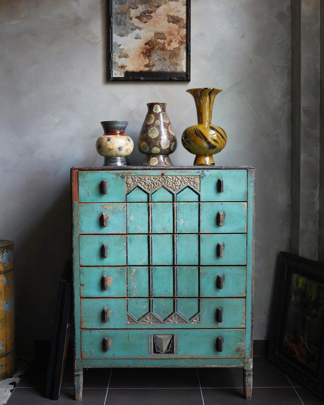Antique turquoise chest of drawers against a grey wall, topped with three decorative vases and a framed picture above.