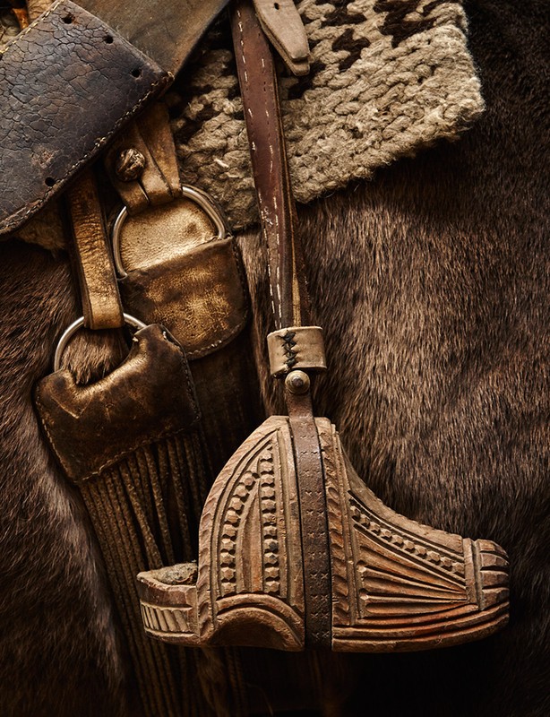 Close-up of leather and wood horse tack, showing a stirrup and part of the saddle. Horse-riding equipment detail, equestrian lifestyle aesthetic.