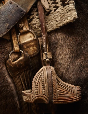 Close-up of leather and wood horse tack, showing a stirrup and part of the saddle. Horse-riding equipment detail, equestrian lifestyle aesthetic.