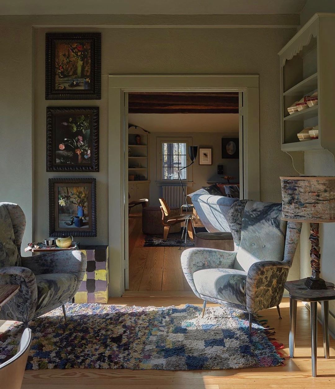 Cozy living room interior with patterned armchairs, a colorful rug, and artwork, bathed in soft natural light, creating a warm, inviting space.