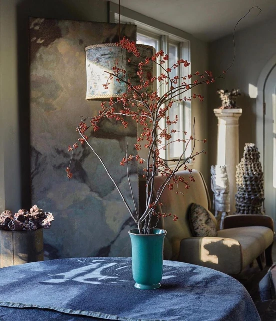 Interior living space featuring a table centerpiece with berries in a vase, complemented by art and vintage furniture in warm lighting.