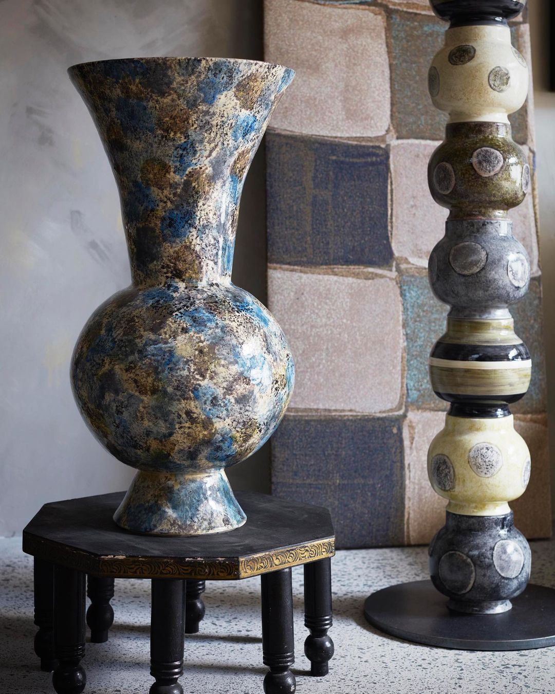 Tall decorative blue and tan ceramic vase with an orb shape displayed on a dark wood pedestal table with a textured background.