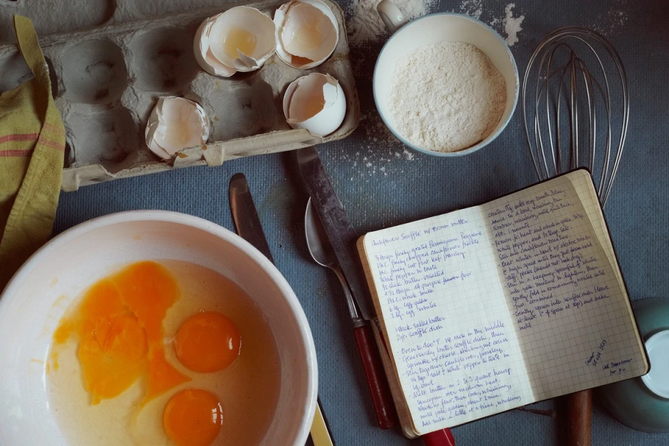 Overhead view of ingredients for baking, including eggs, flour, and a handwritten recipe, suggesting a cozy, homemade cooking scene.