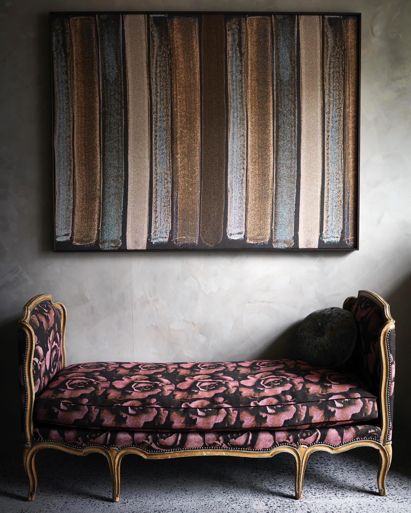 Interior design featuring a floral settee in front of an abstract painting with gray concrete wall providing a modern contrast.
