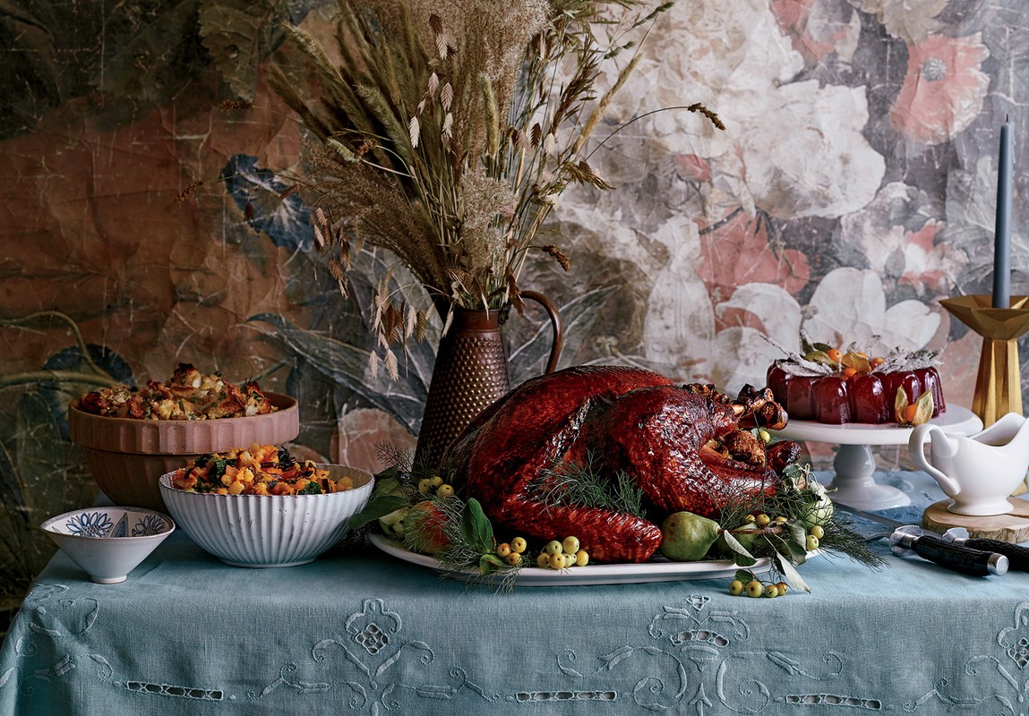 Thanksgiving table featuring a roasted turkey, bowls of stuffing, and cranberry sauce, set against a floral backdrop.