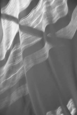 Monochrome photographic study of draped fabric with soft light casting abstract shadows across ripples and folds.