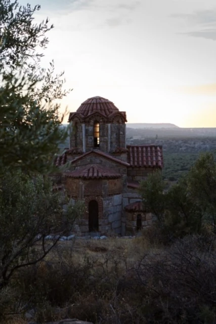 Exterior daytime view of a stone church with a red tile roof and dome surrounded by trees in a rural landscape with a sky.