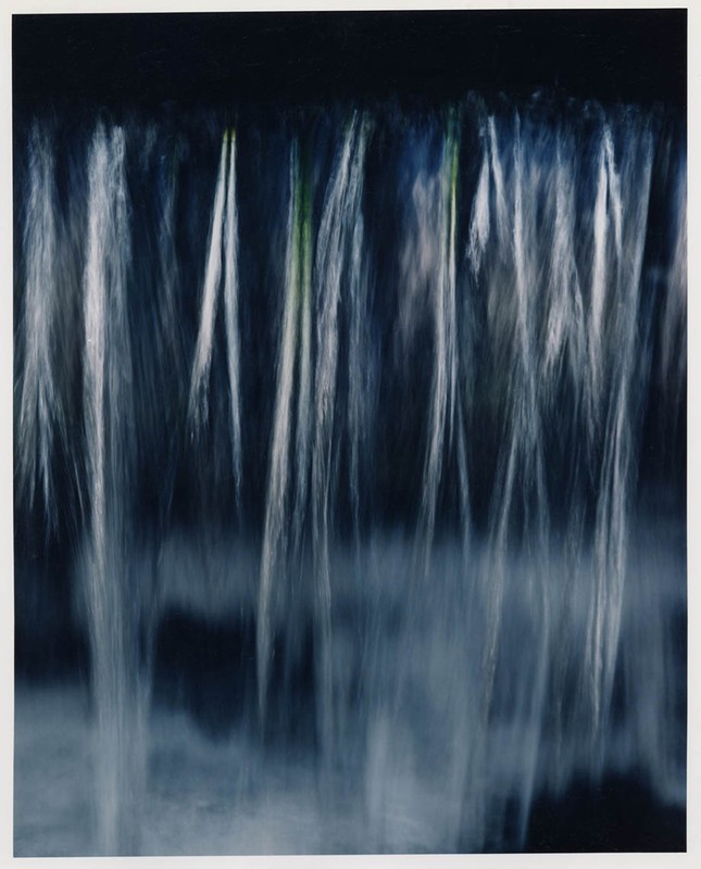 Abstract long exposure of water cascading down a dark surface, creating a blurred, dreamy effect with streaks of light and dark blue.