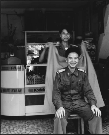 Two smiling men in uniform pose indoors with a film and camera display. One sits while the other holds a garment behind him.