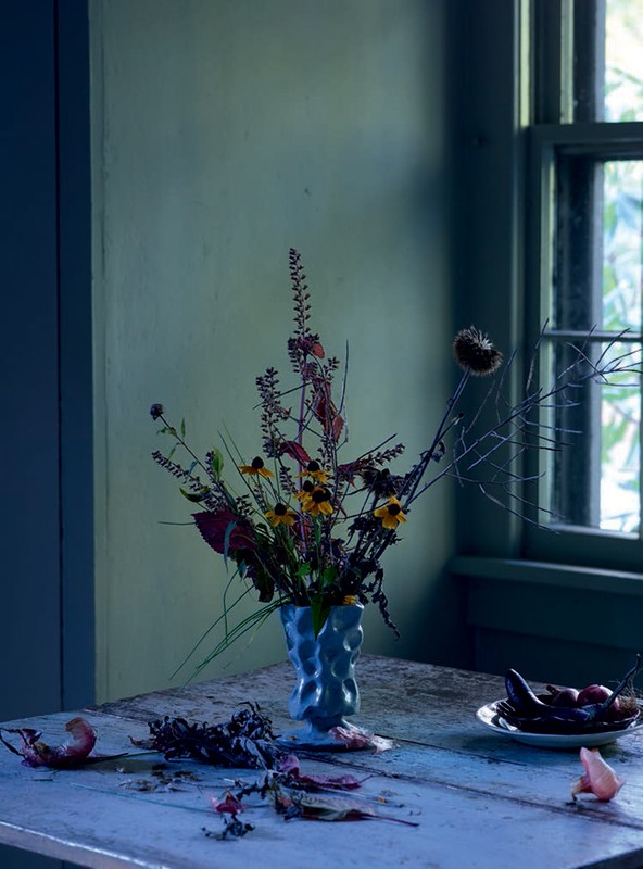 Still life photography of a floral arrangement in a blue vase on a wooden table near a window, capturing a dark and moody ambiance.