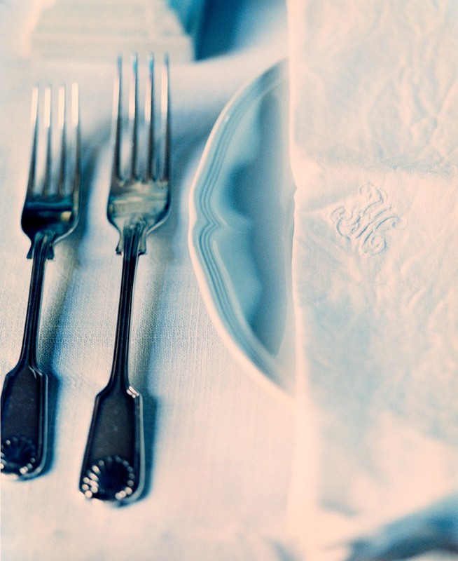 Close-up of two forks, white plate, and monogrammed napkin on white tablecloth, showcasing a table setting.