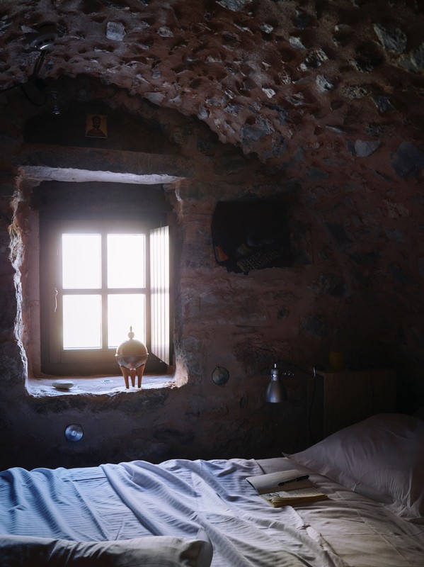 Bedroom interior featuring a bed with striped linens, a window letting in bright light, stone walls, and an antique ceramic object.