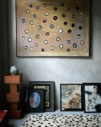 Interior shot featuring a large abstract dotted painting hung on a textured grey wall with several framed artworks on the floor