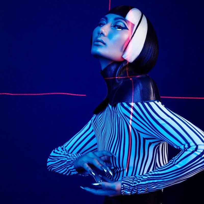 Striking studio portrait of a stylish woman with geometric makeup and futuristic fashion in a dark blue and pink lighted set.