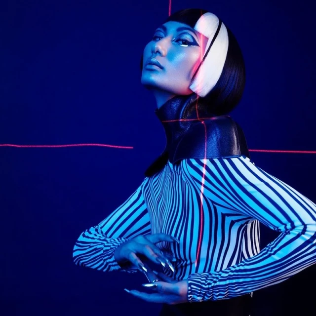 Striking studio portrait of a stylish woman with geometric makeup and futuristic fashion in a dark blue and pink lighted set.
