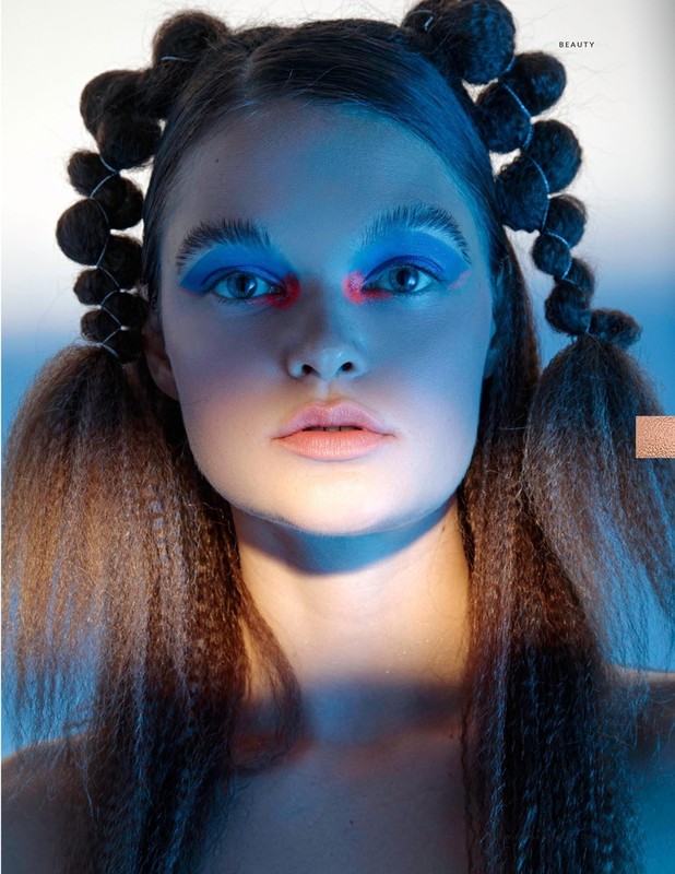 Close-up portrait of a woman with crimped hair styled in space buns, wearing blue eye shadow and red face paint. Beauty, fashion.