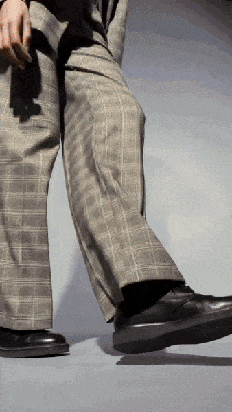 Person in a black top and plaid pants walking in black shoes in a photo studio.