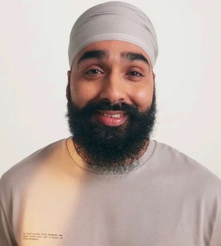 Portrait of a smiling adult man wearing a gray T-shirt and turban against a white background in a studio setting.