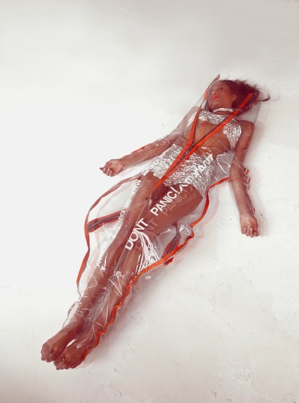Adult female posing while laying in a clear plastic bag with red trim and silver accents on a white background in a studio setting.