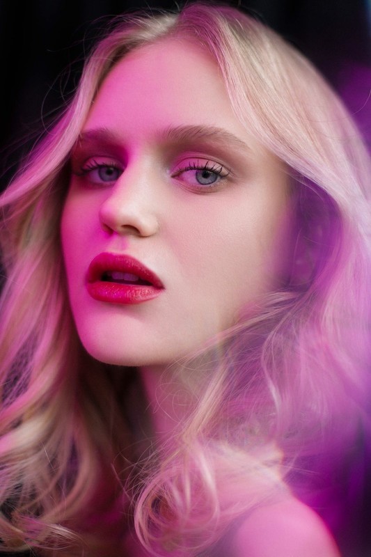 Close-up portrait of a blonde woman with vibrant pink and purple ambient lighting framing her face.