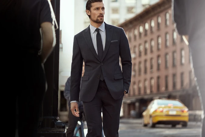 A man in a suit walks along a city street, looking away from the camera. The shot features a shallow depth of field, blurring the background.