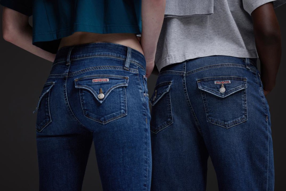 Close-up of two people wearing dark blue jeans with distinctive pocket detailing and cropped shirts, against a neutral background.
