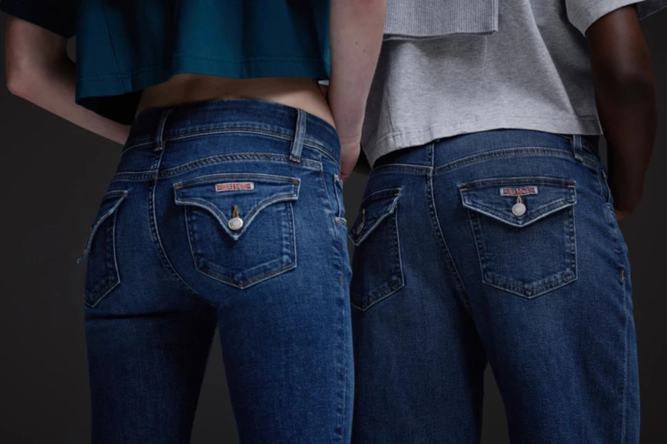 Close-up of two people wearing dark blue jeans with distinctive pocket detailing and cropped shirts, against a neutral background.
