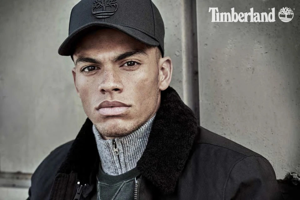 Portrait of a young adult male wearing a Timberland cap and jacket, shot in a neutral studio setting with soft lighting.