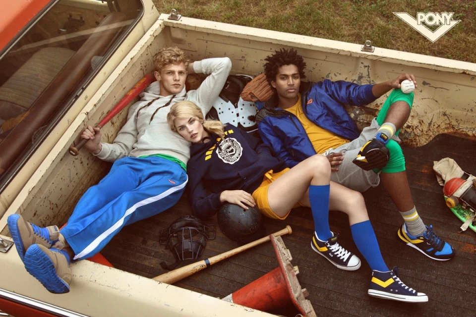 Three fashion models pose in the bed of a truck with vintage baseball gear, showcasing sports-inspired fashion and a retro aesthetic.