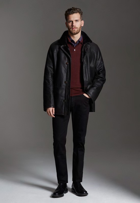 Man wearing a black leather jacket over a burgundy polo shirt and dark trousers against a neutral grey studio background