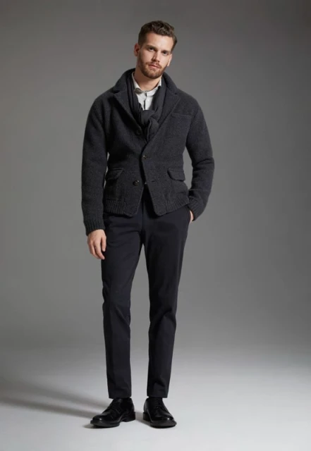 Full-length shot of an adult male wearing a grey jacket, vest, white shirt, dark pants, and black leather shoes, in a studio setting.