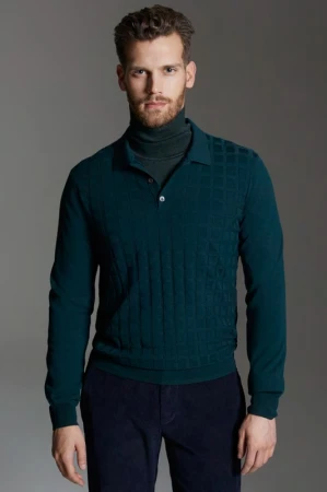 A man wearing a textured dark green polo shirt and dark trousers posed against a plain grey background