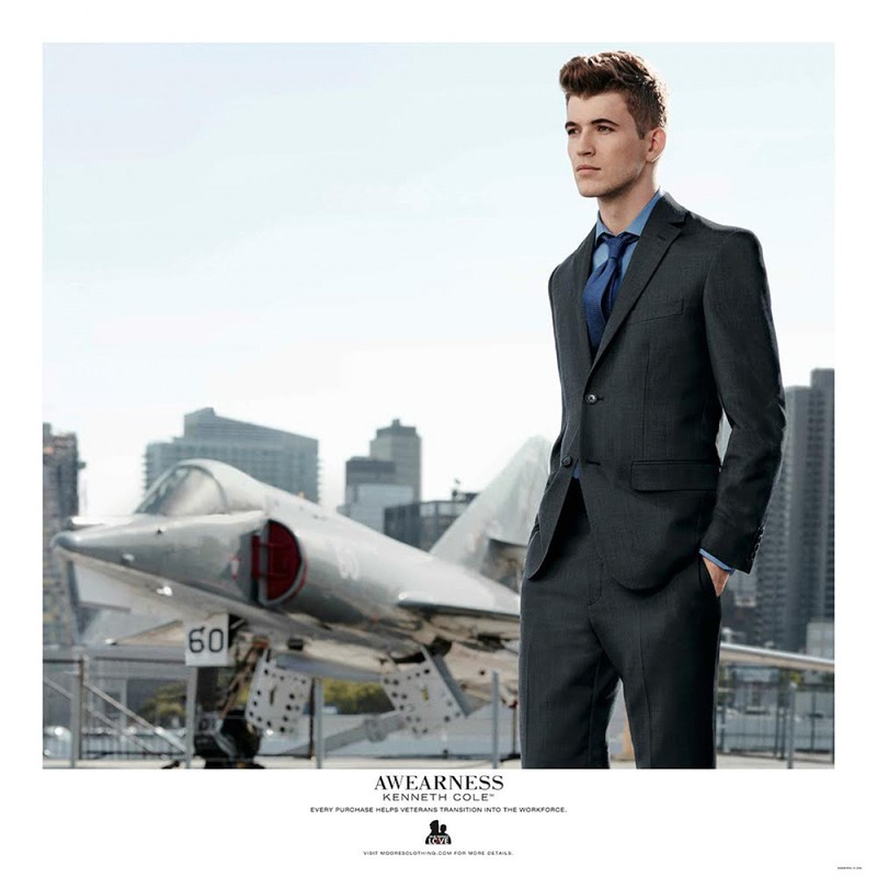 Man in suit stands near jet on aircraft carrier with city skyline backdrop, professional and polished look with a modern military vibe.