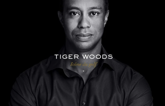 Portrait of Tiger Woods against a black background with white and gold text. Focus on his face and shoulders.