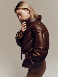 Blonde woman wearing a glossy brown leather puffer jacket posing against a plain neutral background