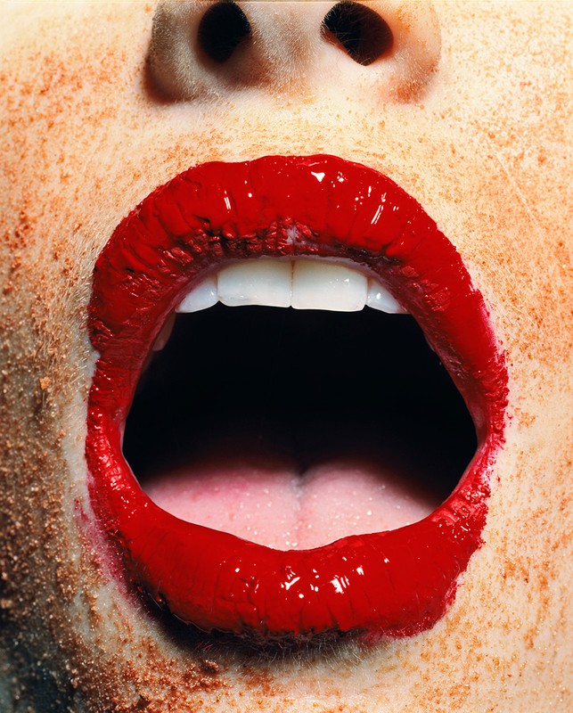 Close-up of a person's open mouth with red lipstick on their lips, white teeth visible, and freckles around the mouth and nose.