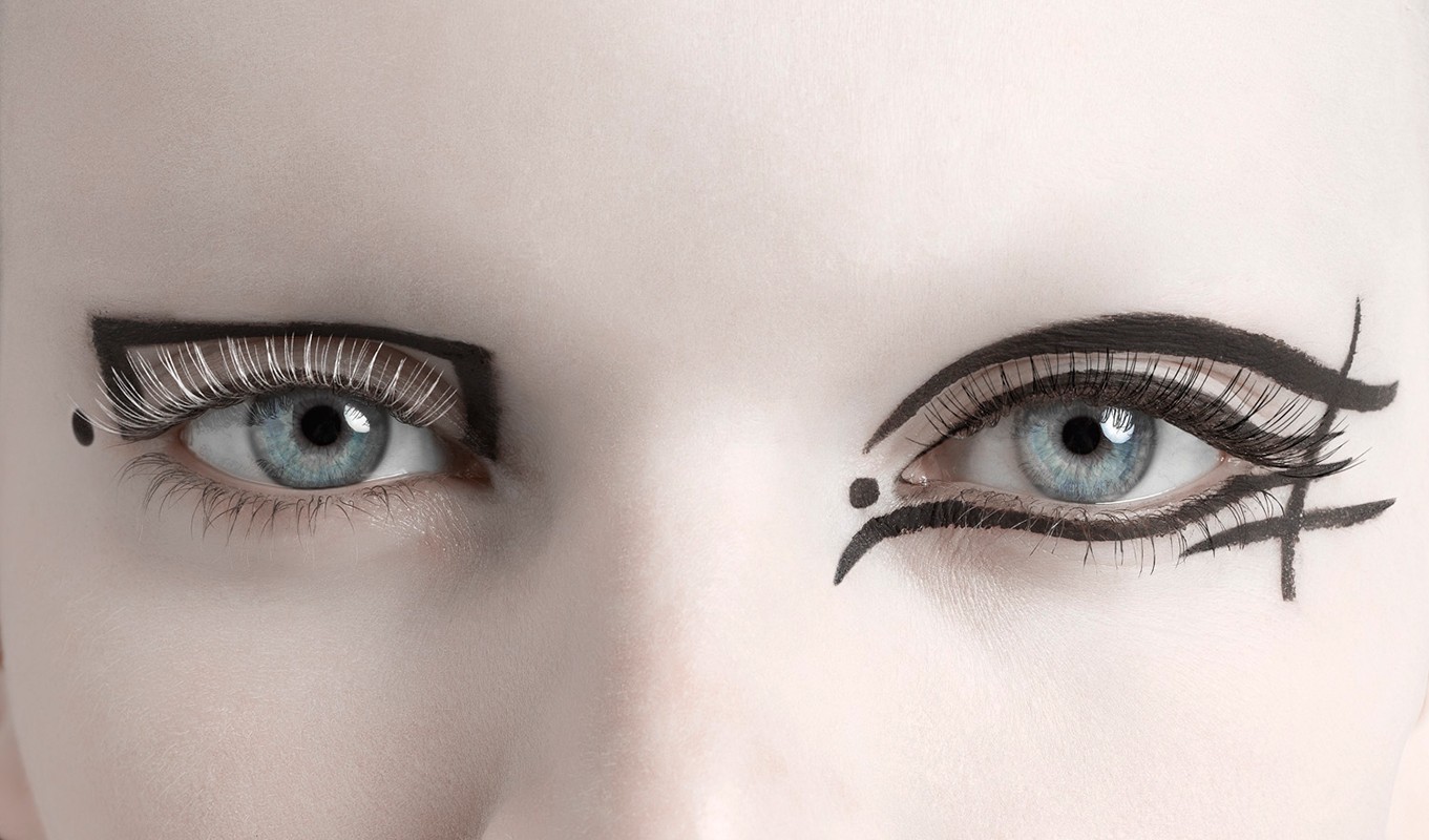 Close-up of a fair-skinned woman's face with bold black graphic eye makeup on each eye and long eyelashes. Studio lighting.