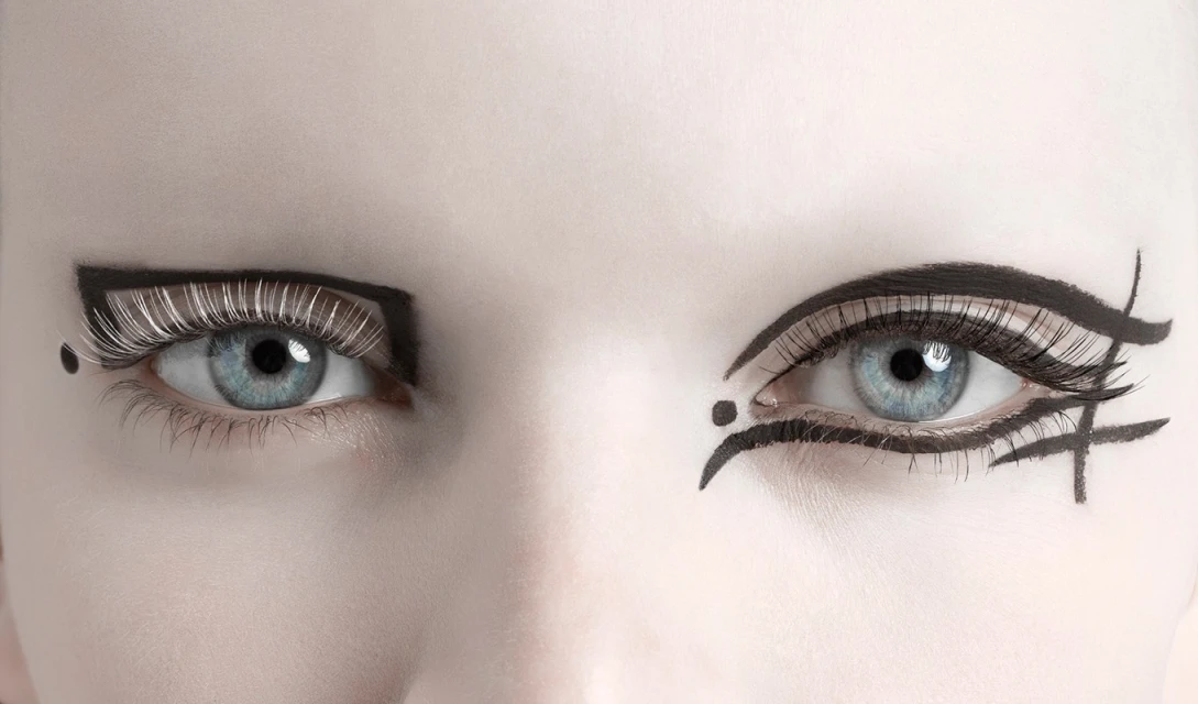 Close-up of a fair-skinned woman's face with bold black graphic eye makeup on each eye and long eyelashes. Studio lighting.