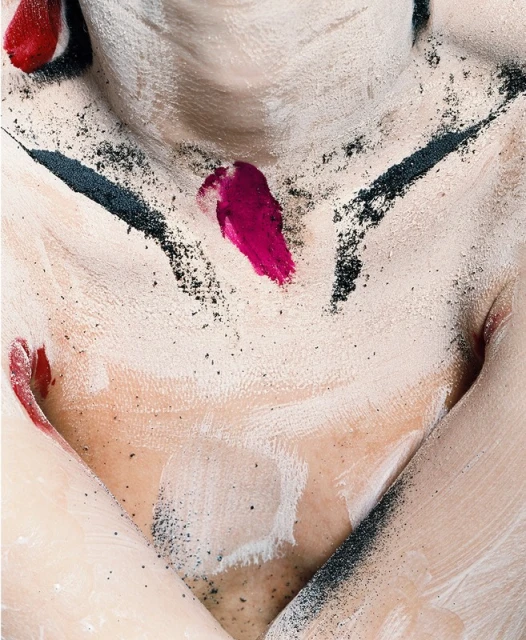 Close-up shot of a model's torso covered in white paint and black powder, accented with vivid red paint streaks, creating a textured, artistic effect.