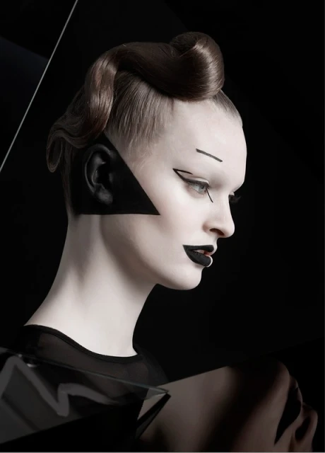 Profile of a woman with stylized makeup and a geometric black design, featuring a sleek updo hairstyle against a dark background.