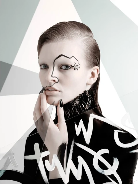 A young adult female model poses with black and white body paint, nail polish, lace collar, and slicked-back hair in front of a geometric background.