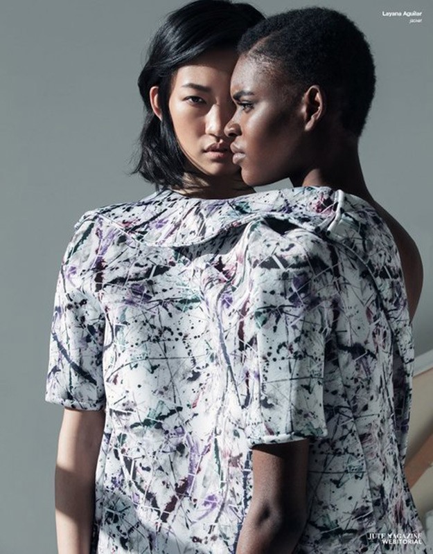 Two women with dark hair are closely posed in front of a light gray studio backdrop. The woman in the front wears a patterned top.