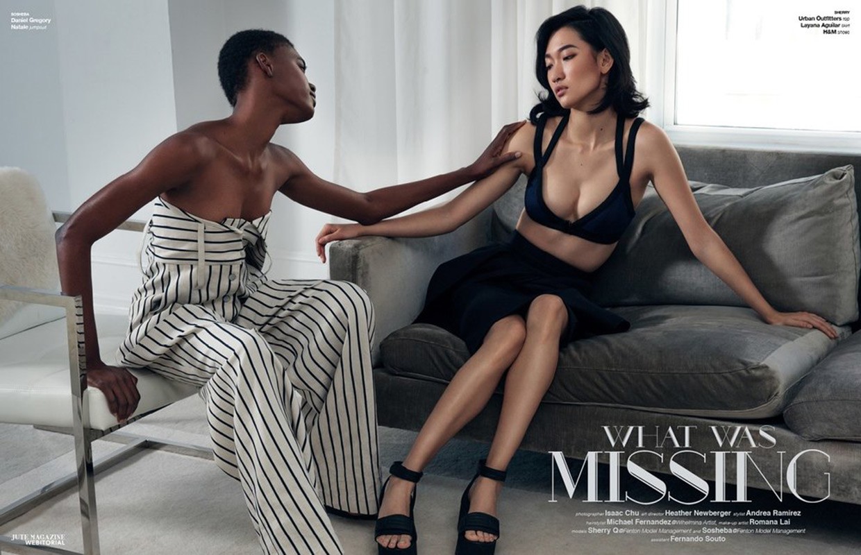 Two fashion models posing together in a bright interior space with minimalist furniture and white sheer curtains.
