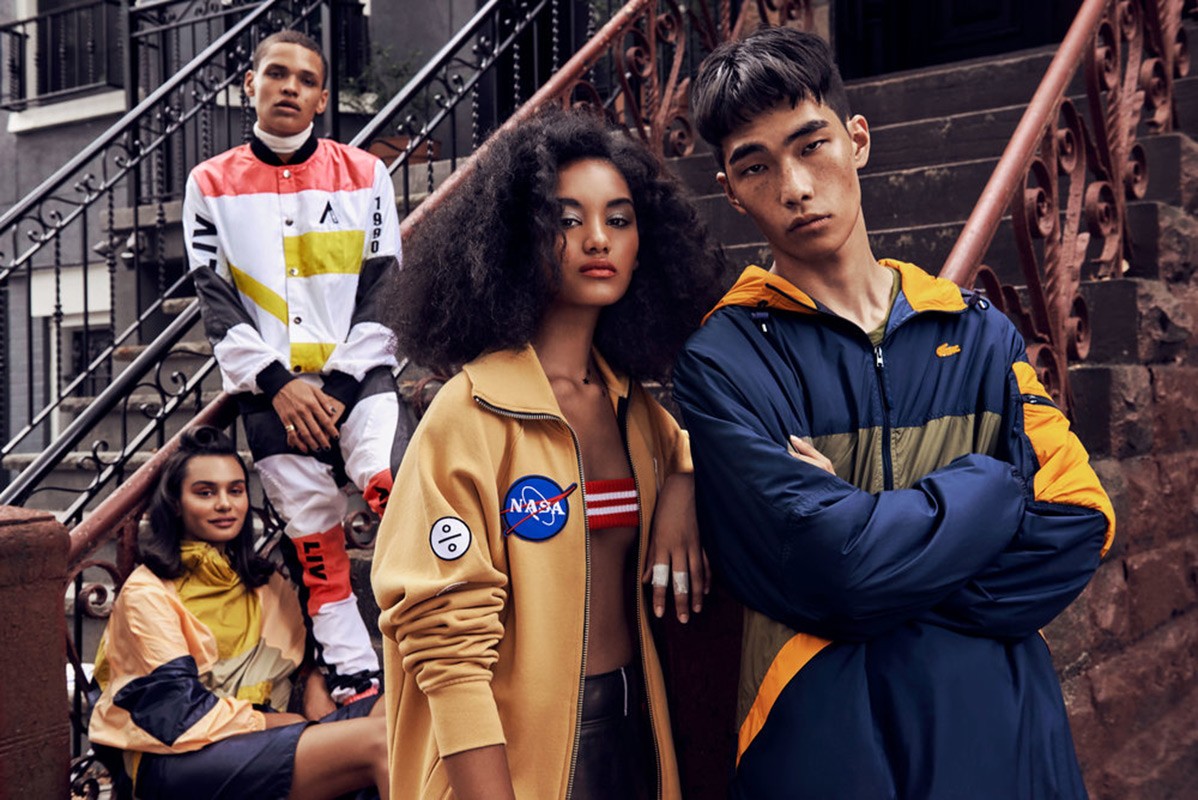 Four diverse fashion models pose on brownstone steps wearing color-blocked jackets. Urban setting, medium shot, commercial fashion photography.