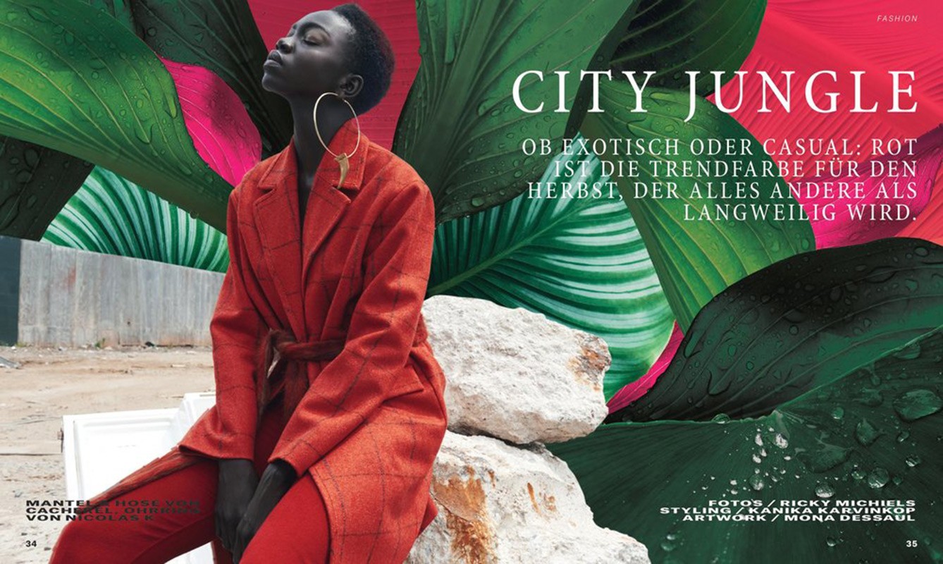 Woman in red coat poses outdoors in front of green tropical leaves and rock formations in a fashion editorial with vibrant colors.