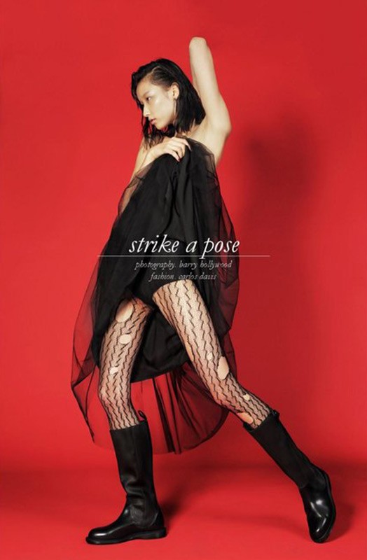 Model in black tulle skirt and patterned tights holding fabric against a solid red background