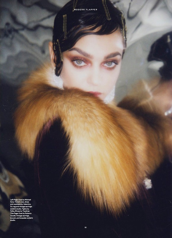 Editorial fashion portrait of a woman with dark hair and gold hairpins wearing a fur stole against a reflective background.